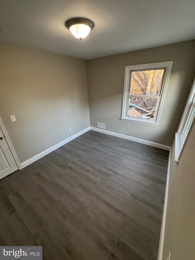 spare room featuring dark wood-style floors, visible vents, and baseboards