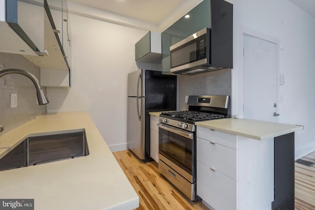 kitchen with stainless steel appliances, light countertops, light wood-style floors, white cabinetry, and a sink