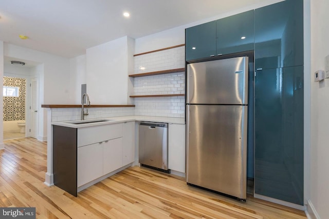 kitchen with light wood finished floors, open shelves, stainless steel appliances, decorative backsplash, and a sink