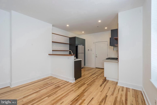 kitchen with open shelves, a peninsula, freestanding refrigerator, and light wood-style floors