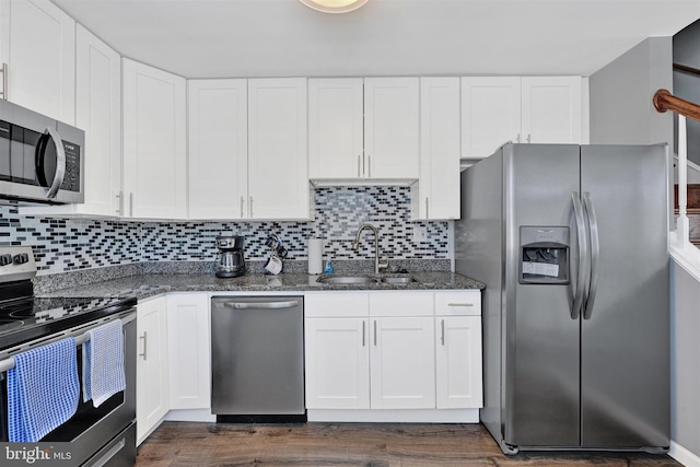 kitchen with dark stone countertops, dark wood finished floors, a sink, stainless steel appliances, and white cabinets