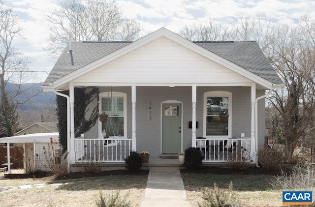 bungalow featuring covered porch, roof with shingles, and brick siding