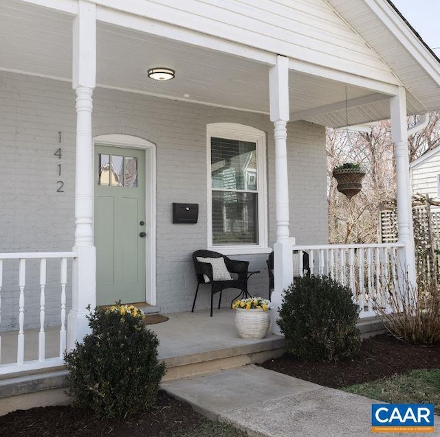 view of exterior entry with a porch and brick siding