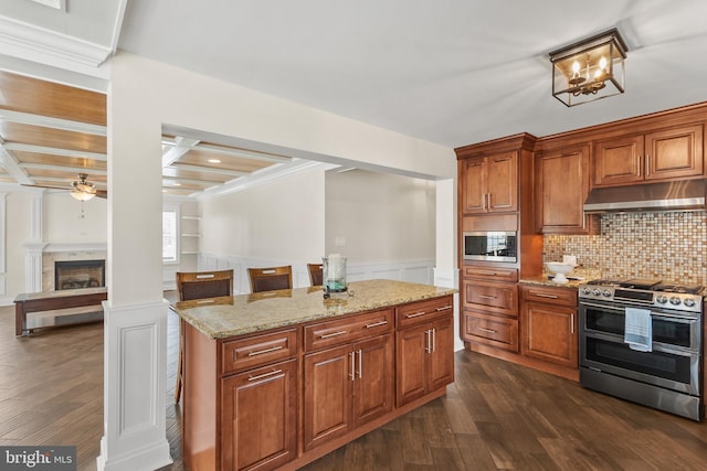 kitchen with dark wood-style floors, a wainscoted wall, appliances with stainless steel finishes, light stone countertops, and under cabinet range hood