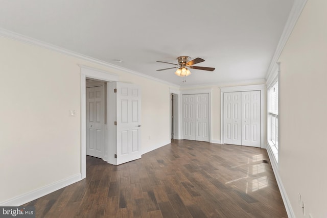 unfurnished bedroom with ornamental molding, dark wood finished floors, two closets, and baseboards