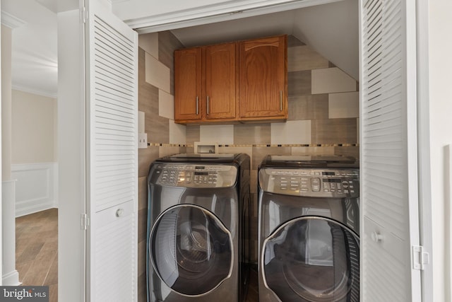 clothes washing area featuring cabinet space, wainscoting, ornamental molding, wood finished floors, and separate washer and dryer