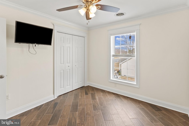 unfurnished bedroom featuring visible vents, baseboards, ornamental molding, a closet, and wood tiled floor