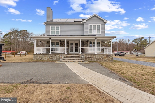 view of front of home featuring ceiling fan, roof mounted solar panels, a porch, and french doors