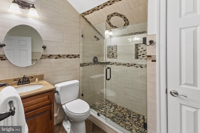 bathroom featuring toilet, a stall shower, vanity, and tile walls