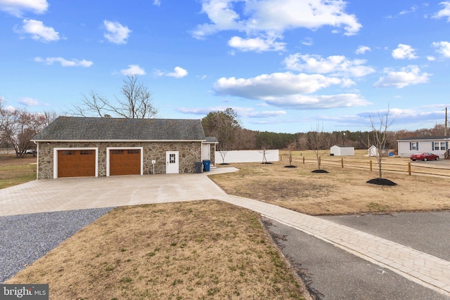 view of front of property featuring decorative driveway, stone siding, fence, and a front lawn