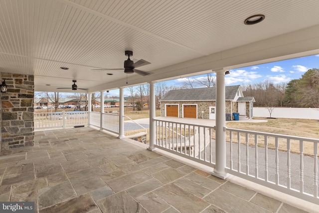 view of patio featuring a garage, driveway, a ceiling fan, an outbuilding, and fence