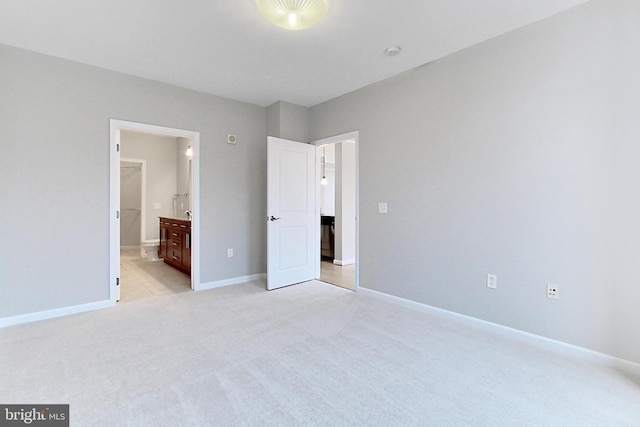 unfurnished bedroom featuring light colored carpet, ensuite bathroom, and baseboards