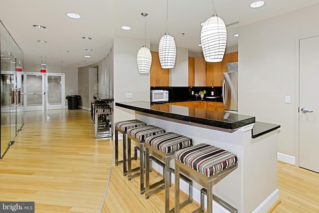 kitchen featuring white microwave, dark countertops, a breakfast bar, light wood-type flooring, and freestanding refrigerator