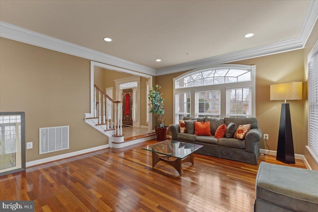 living room featuring stairs, crown molding, visible vents, baseboards, and hardwood / wood-style flooring