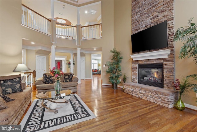 living area with baseboards, a stone fireplace, wood finished floors, and ornate columns