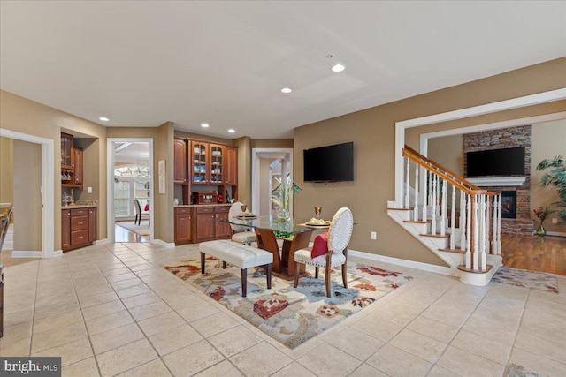 dining space with recessed lighting, light tile patterned flooring, a stone fireplace, baseboards, and stairs