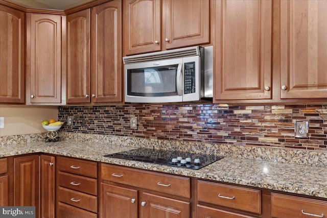 kitchen featuring light stone counters, tasteful backsplash, stainless steel microwave, and black electric cooktop