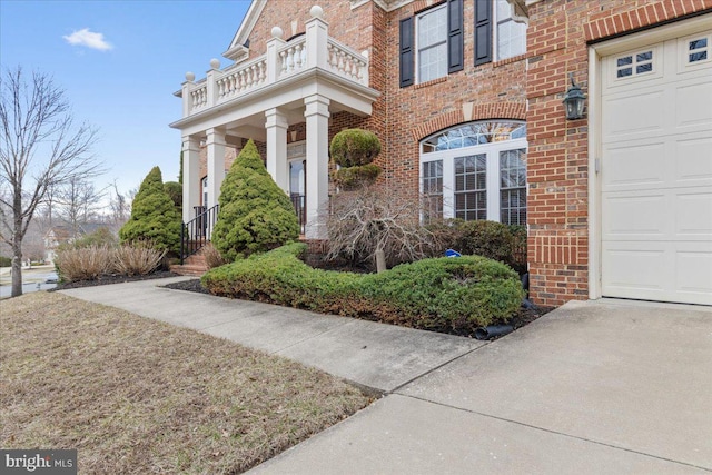 entrance to property featuring a garage, brick siding, and a balcony