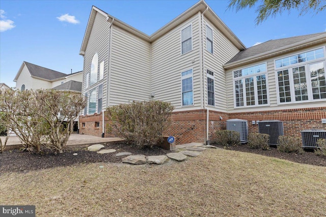 view of side of property with brick siding, a patio, a lawn, and central air condition unit