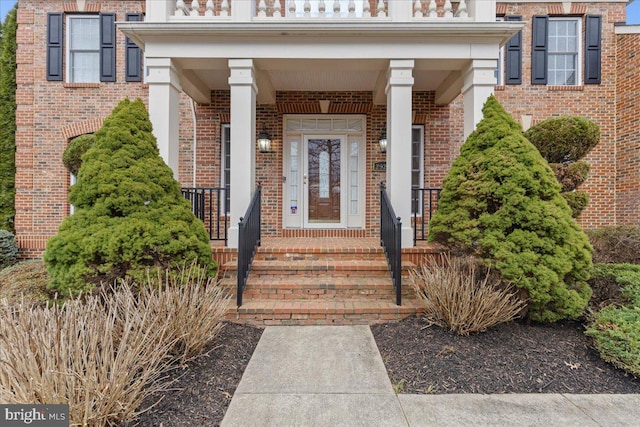 view of exterior entry with brick siding and a balcony