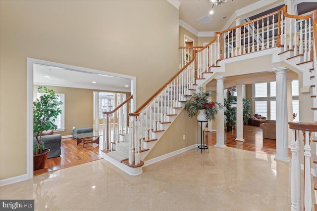 entryway featuring ornate columns, a high ceiling, baseboards, and crown molding