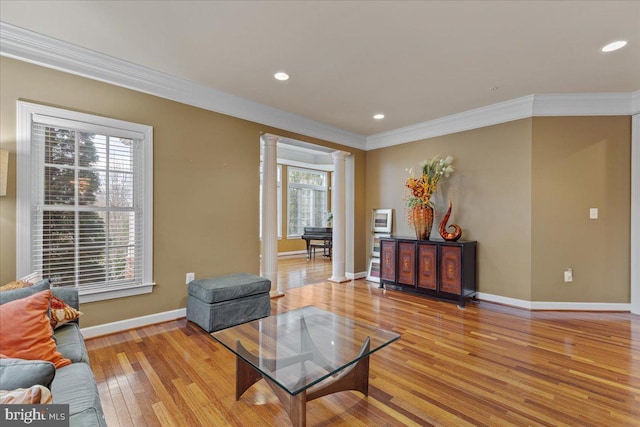 living area featuring crown molding, light wood finished floors, recessed lighting, ornate columns, and baseboards