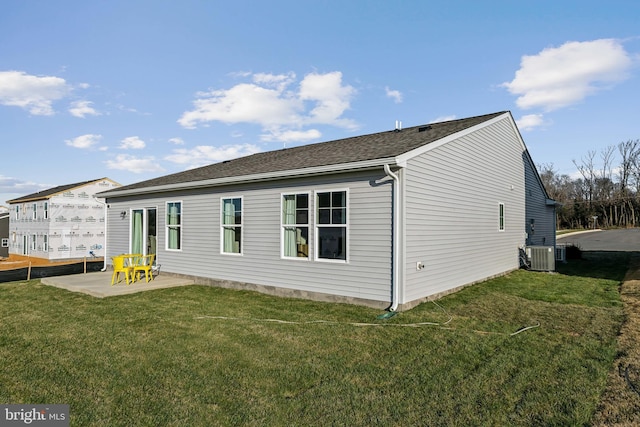 rear view of house with central AC, roof with shingles, a lawn, and a patio area