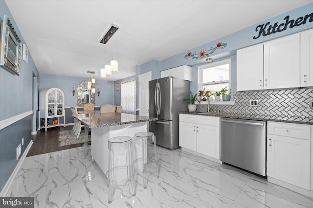 kitchen featuring a sink, a kitchen breakfast bar, dark stone counters, appliances with stainless steel finishes, and white cabinets