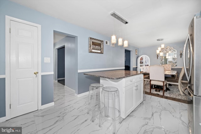 kitchen with a breakfast bar, marble finish floor, freestanding refrigerator, an inviting chandelier, and white cabinets