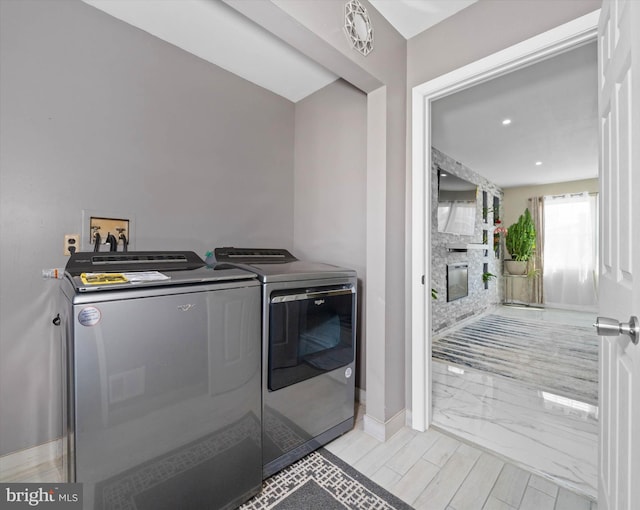 laundry area with light wood-style floors, a fireplace, baseboards, laundry area, and washing machine and clothes dryer