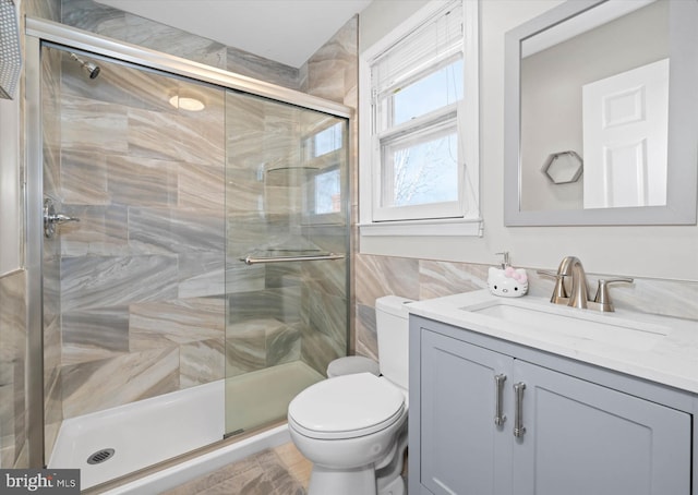 bathroom featuring tile walls, a stall shower, toilet, and vanity