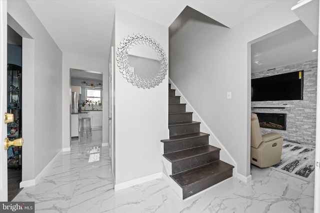 stairway featuring a stone fireplace, baseboards, and marble finish floor