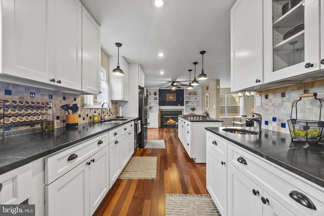 kitchen with dark countertops, white cabinetry, a sink, and a glass covered fireplace