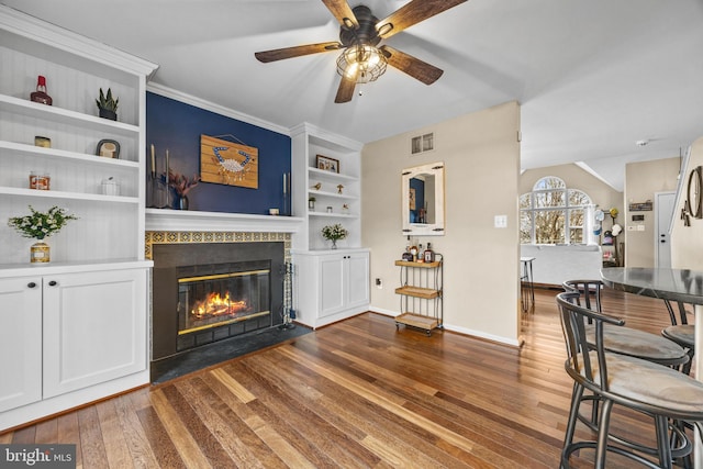 living room featuring built in features, a glass covered fireplace, visible vents, and wood finished floors