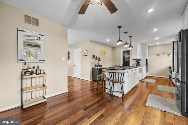 kitchen with a breakfast bar area, dark wood-style flooring, visible vents, white cabinets, and freestanding refrigerator