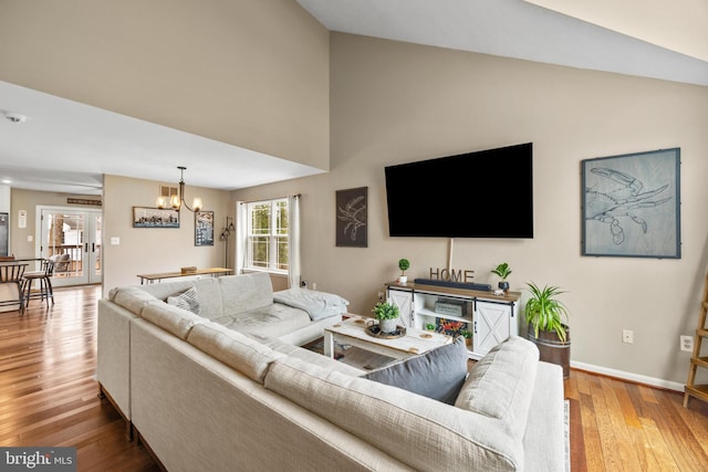 living room with a chandelier, lofted ceiling, baseboards, and wood finished floors