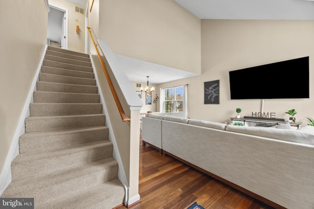 staircase with visible vents, an inviting chandelier, wood finished floors, high vaulted ceiling, and baseboards