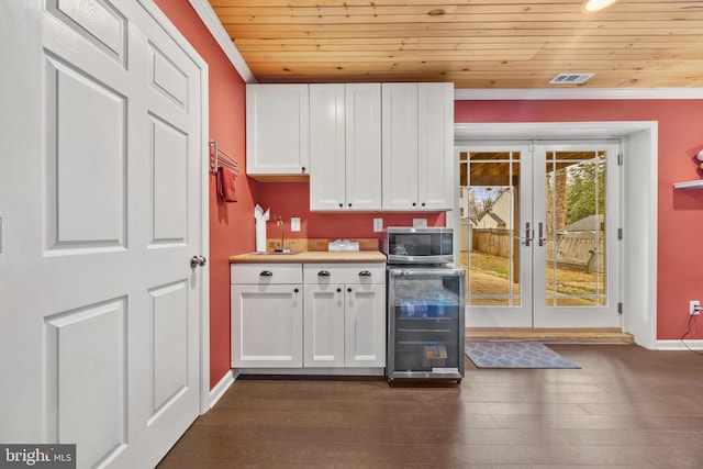 kitchen with dark wood-style floors, wine cooler, stainless steel microwave, white cabinetry, and a sink