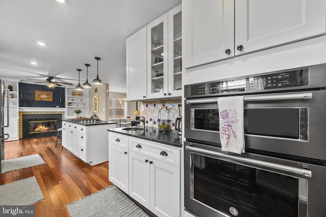 kitchen featuring white cabinets, a glass covered fireplace, dark countertops, wood-type flooring, and a sink