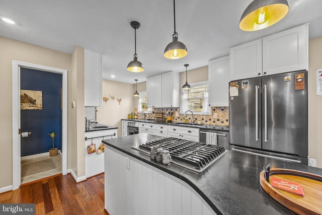 kitchen featuring dark wood finished floors, dark countertops, stainless steel appliances, white cabinetry, and a sink