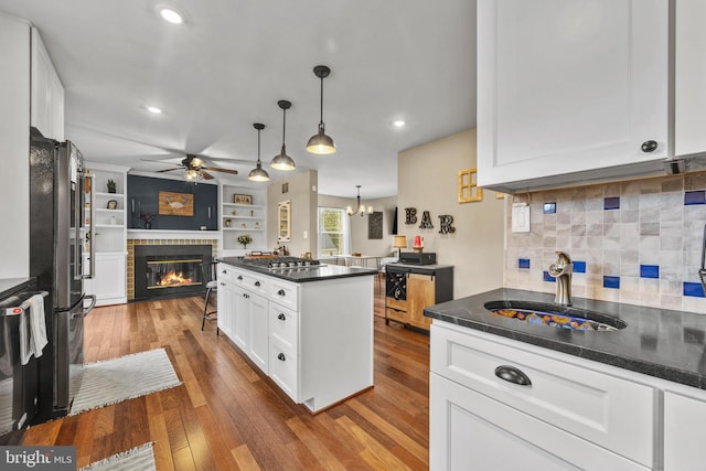 kitchen with hardwood / wood-style flooring, a sink, open floor plan, appliances with stainless steel finishes, and a glass covered fireplace