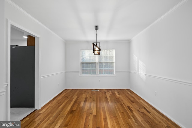 unfurnished dining area featuring baseboards, ornamental molding, and wood finished floors