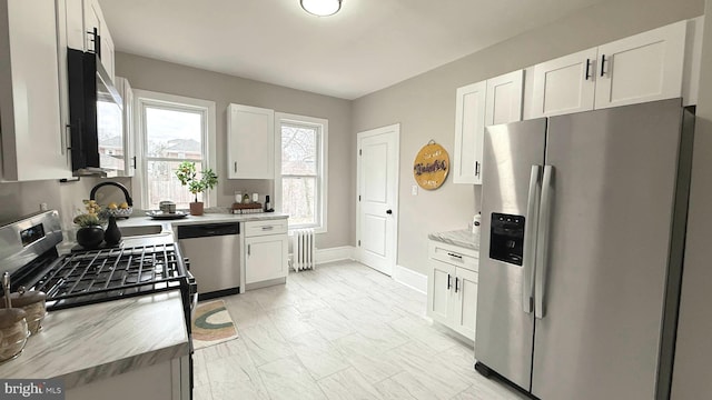 kitchen with stainless steel appliances, radiator heating unit, white cabinets, a sink, and baseboards