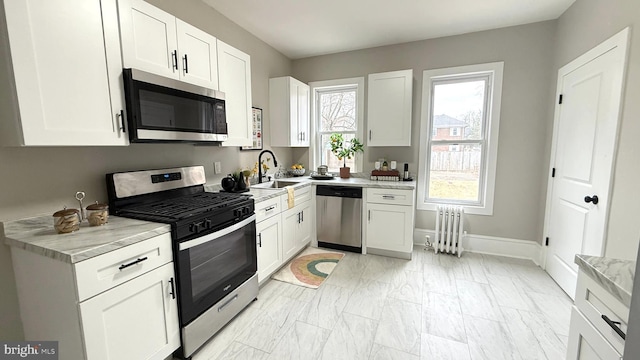 kitchen with appliances with stainless steel finishes, radiator heating unit, plenty of natural light, and a sink