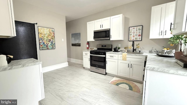 kitchen featuring marble finish floor, light countertops, appliances with stainless steel finishes, white cabinetry, and a sink