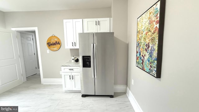 kitchen with marble finish floor, white cabinets, light stone countertops, stainless steel fridge, and baseboards