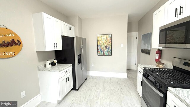 kitchen with white cabinetry, appliances with stainless steel finishes, light stone counters, and baseboards