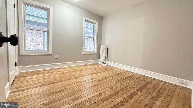 unfurnished room featuring radiator, light wood-style flooring, and baseboards