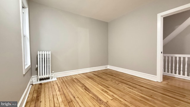 empty room featuring radiator heating unit, wood-type flooring, and baseboards