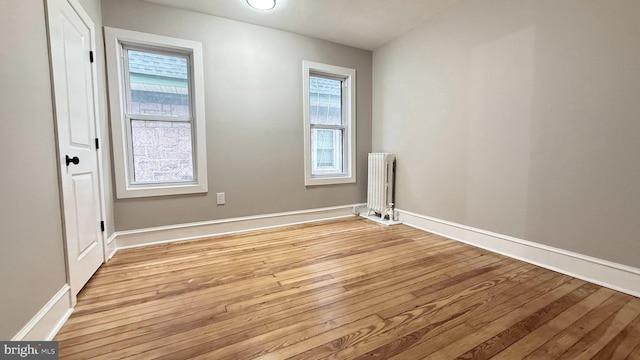 empty room with radiator, light wood finished floors, and baseboards